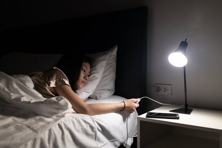 A young girl touches the light switch of a lamp on her bedside table.