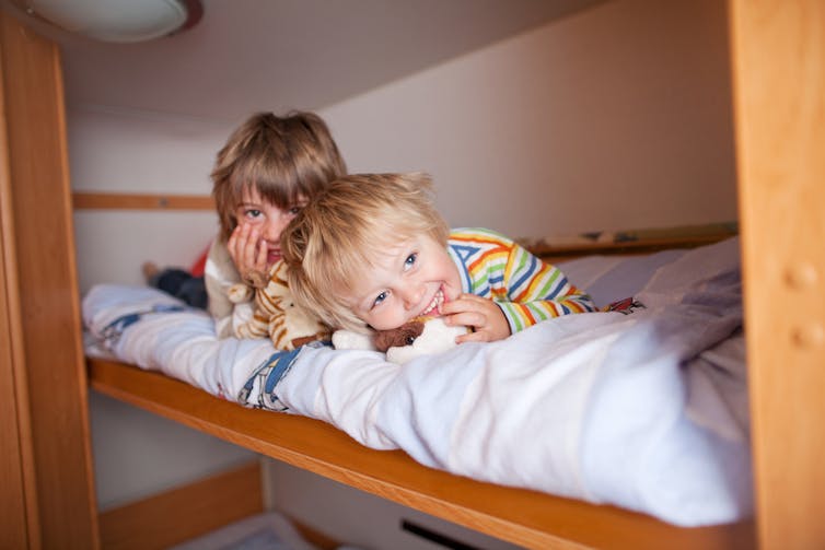 Two children peek out from a bunk bed.