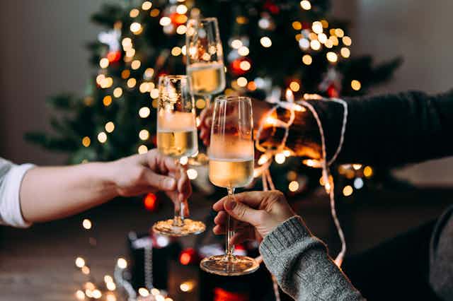 Three people clinking champagne glasses in front of Christmas tree with fairy lights on tree