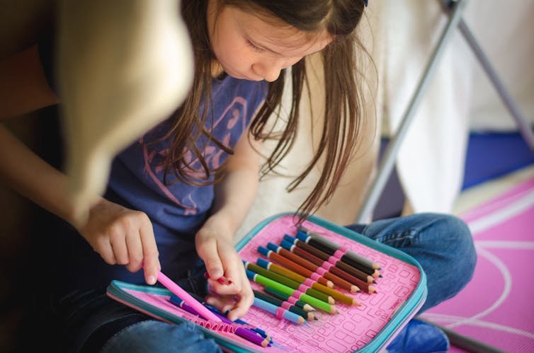 A girl looks at a set of coloured pencils.