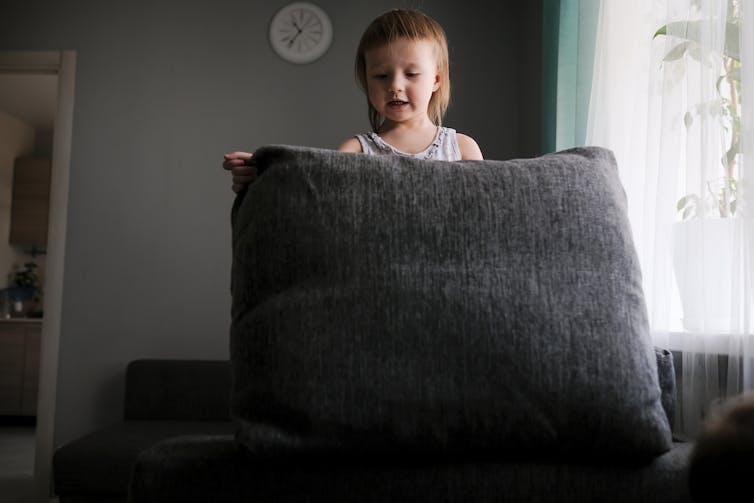 A child plays with a couch cushion.