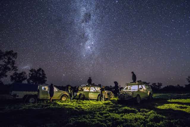 Several people at night watching the stars while near their cars