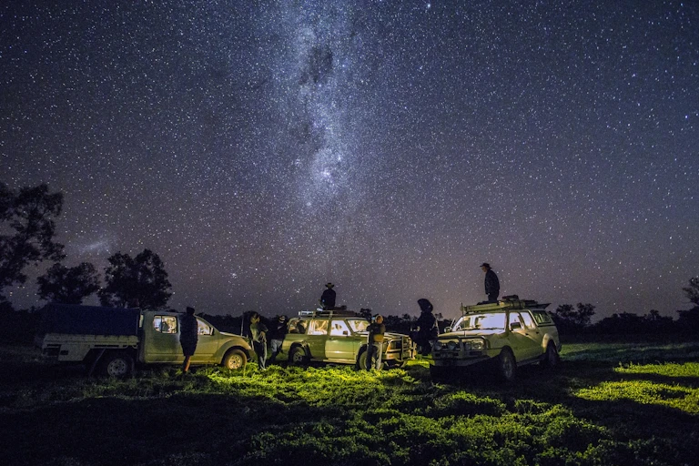 Several people at night watching the stars while near their cars