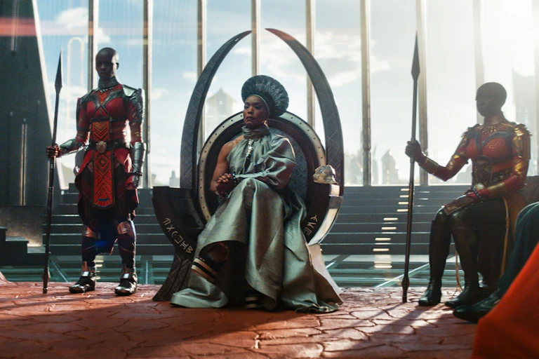 A futurist scene with a queen sitting on a throne with tusk-like shapes at the back of it. Two shaven-headed women in uniform hold spears, guarding her.