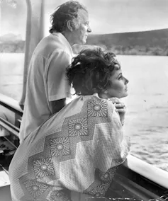 A glamorous couple on the deck of a luxury yacht looking out to sea.