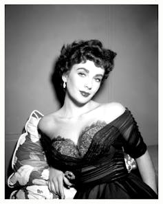 A very glamorous dark-haired young woman in a revealing dress and come hither expression.