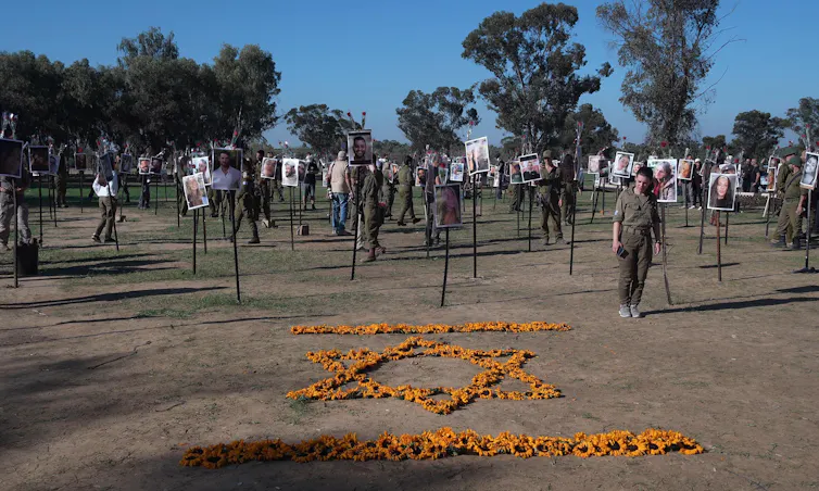 A Star of David made out of sunflower heads on the floor in front of photo portraits on sticks.