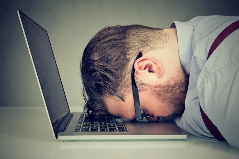Man with shirt, braces and glasses with head down on laptop keyboard.