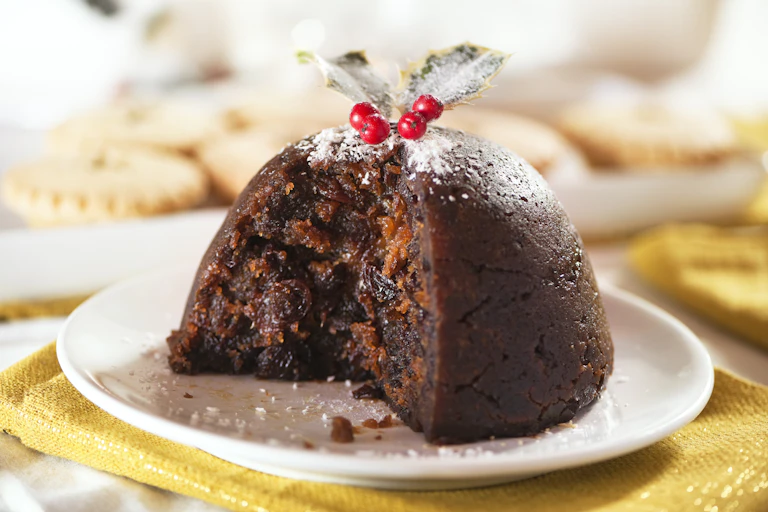 A Christmas pudding, from which a slice has been cut, revealing its raisin-filled rich interior.