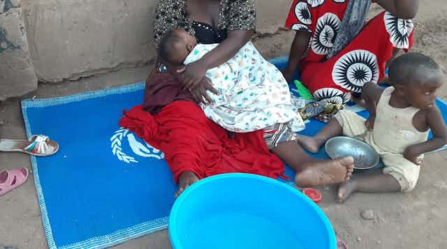 Two women sit with infants on a UN blue mat.
