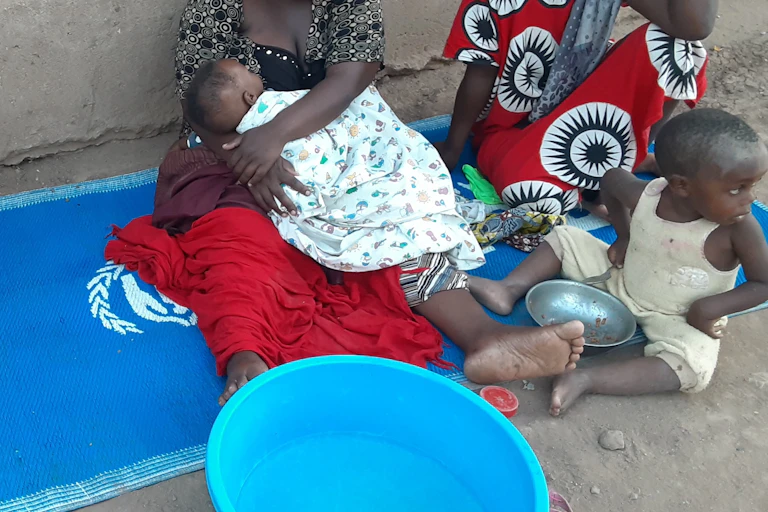Two women sit with infants on a UN blue mat.