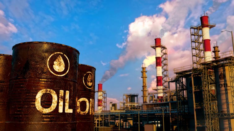 Barrels of oil with an industrial plant in the background, blue sky and clouds or smoke.