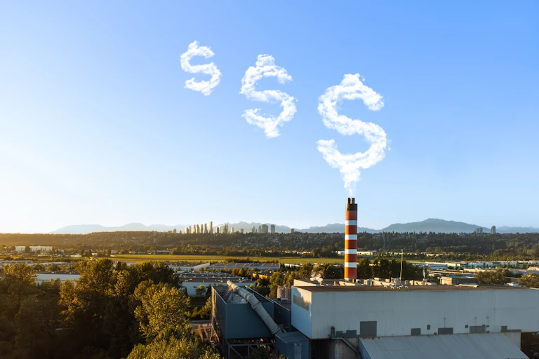 Smokestack with emissions clouds shaped like dollar signs floating into the sky, mountains in the background.