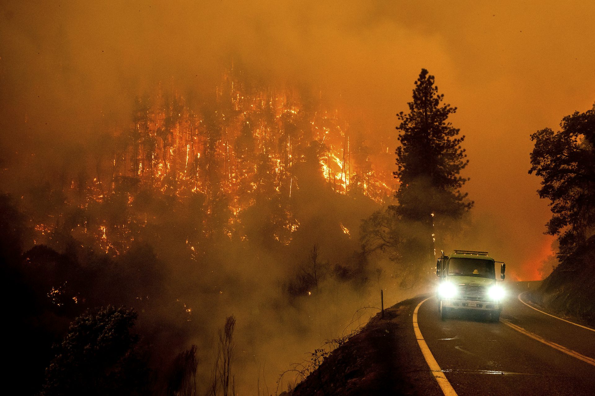A truck drives towards the camera with a burning hillside in the background.