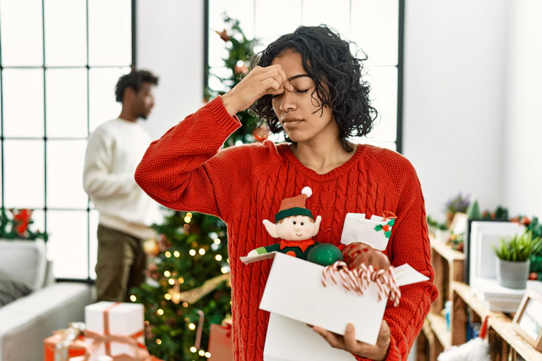 A young woman wearing an elf sweater rests her hand against her face, with her eyes closed, looking stressed.