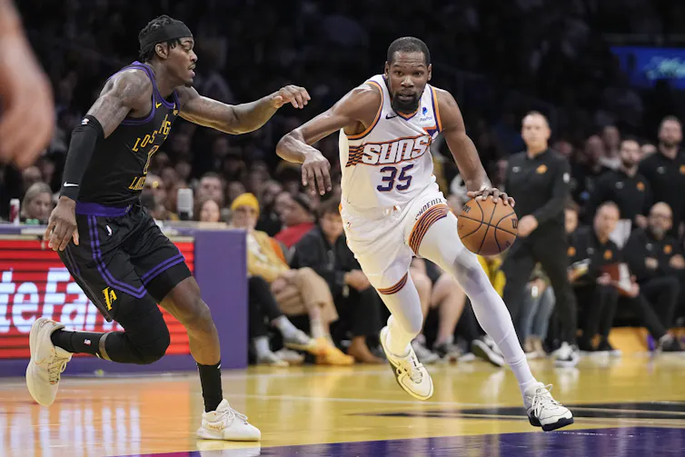 A basketball player dribbles the ball past another basketball player