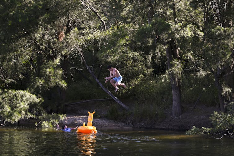 A young man jumps from a tree into a river