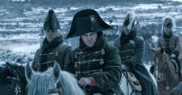 Joaquin Phoenix as Napoleon on horseback against a snowy background with his men.