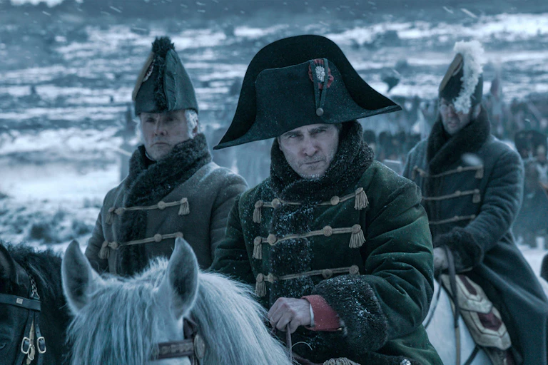 Joaquin Phoenix as Napoleon on horseback against a snowy background with his men.