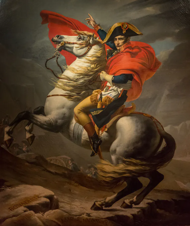 An early 19th-century painting of Napoleon Bonaparte wearing a red cape sitting on a rearing horse.