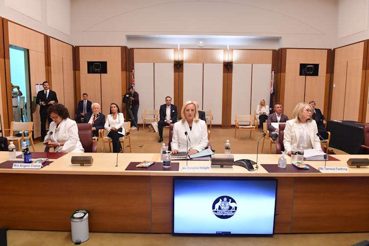 Three women sit behind a large wooden desk in a senate inqury