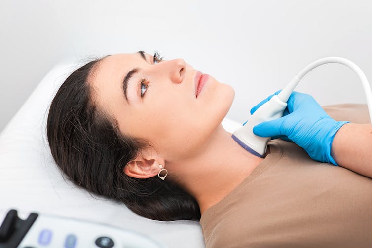 woman lies on exam table getting ultrasound of lower neck