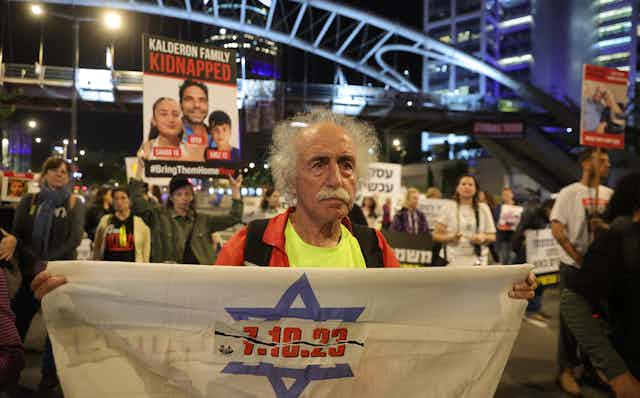 An elderly man holds up a banner saying: 7.10.23 at a demonstration by the families of hostages in Tel Aviv, December 2023