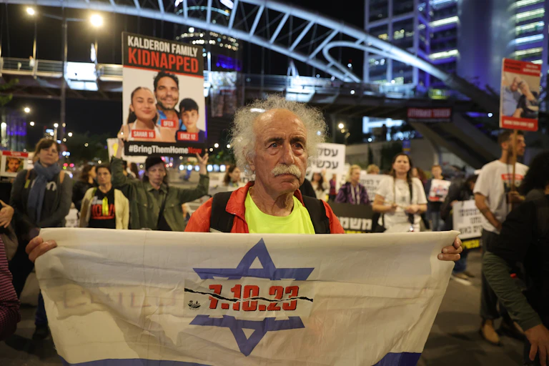 An elderly man holds up a banner saying: 7.10.23 at a demonstration by the families of hostages in Tel Aviv, December 2023