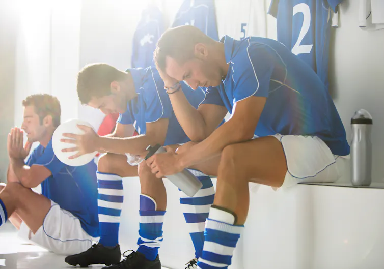 Three football players sit in disappointment in the locker room.