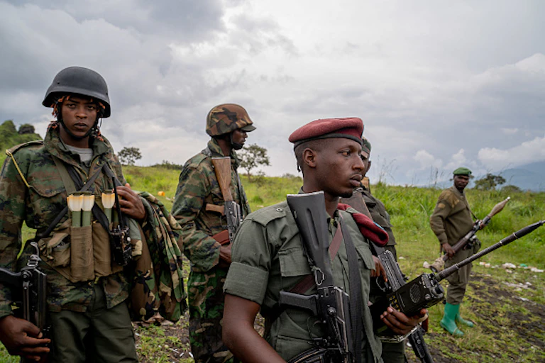 Five soldiers armed with automatic weapons and an RPG standing in the bush.