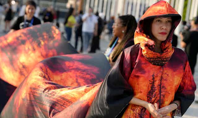 A woman seen in a billowing dress with a long train printed with wildfire.