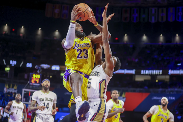 A basketball player jumps while holding a basketball while another player tries to hit the ball out of his hands