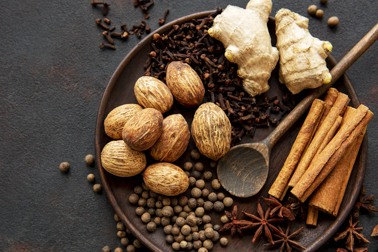 Dried nutmeg fruits and cinnamon sticks, fresh ginger and other spices on a plate