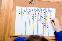 A student's hand seen putting pins under different categories of numbers on a board.