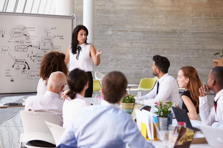 An Asian woman giving a presentation to a group of people using a whiteboard