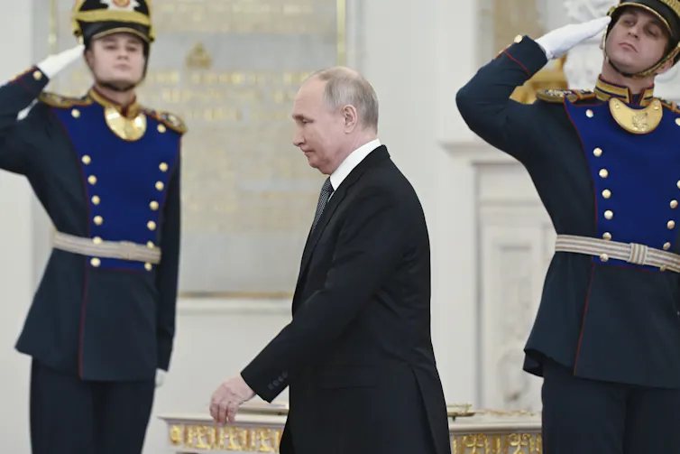 Putin walks past two saluting Russian soldiers.