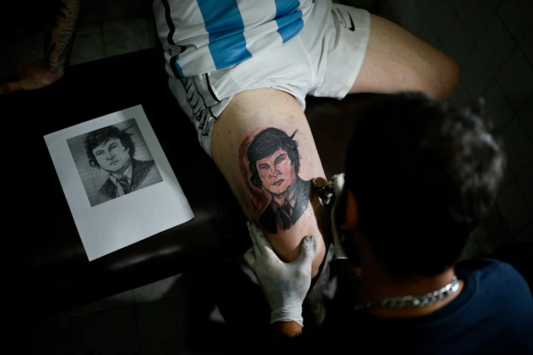 Tatoueur en train de tatouer le visage de Javier Milei sur la cuisse d'un. homme en maillot de l'équipe nationale de football d'Argentine