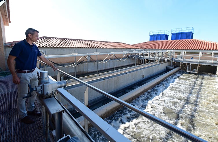 A man stands on a walkway overlooking wastewater in a small treatment facility.