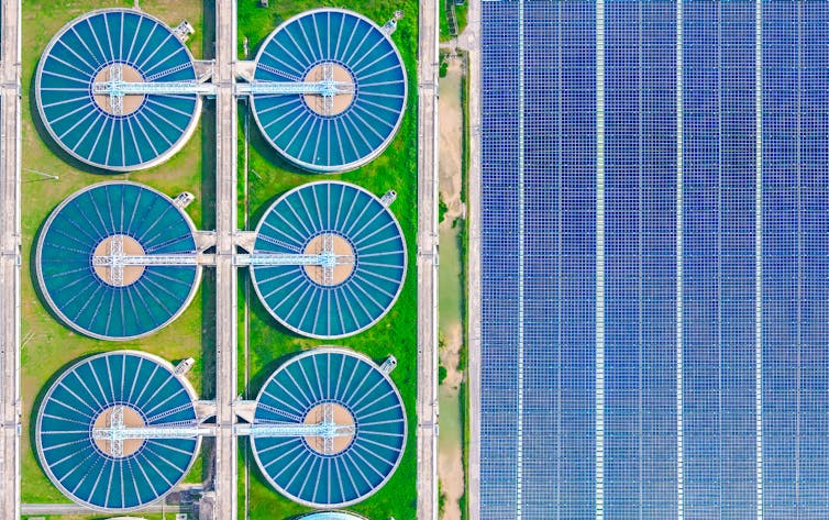 An overhead view of 6 round water treatment tanks at a large water treatment facility next to solar panels.