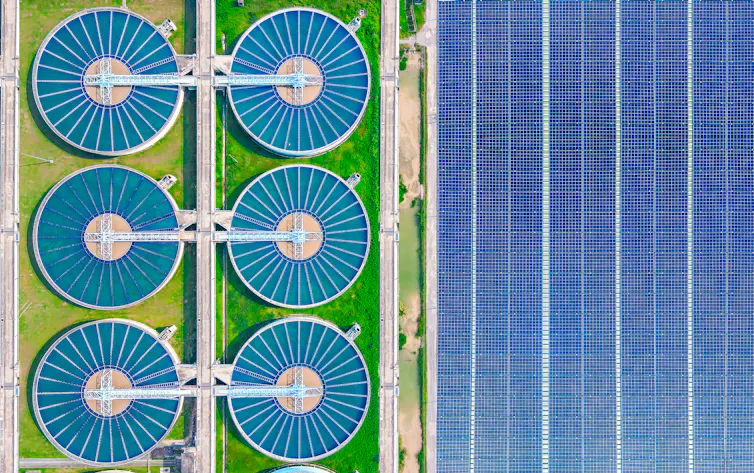 An overhead view of 6 round water treatment tanks at a large water treatment facility next to solar panels.