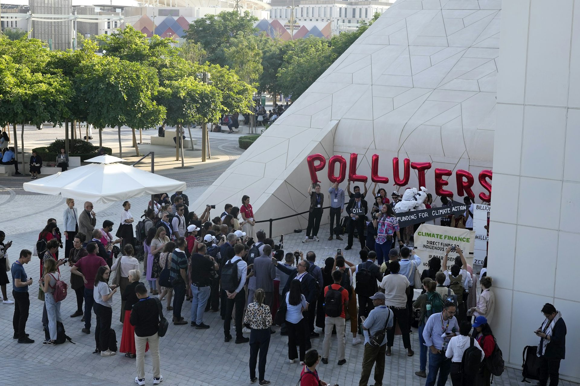 People seen milling around a demonstration where a large sign that says polluters is seen.