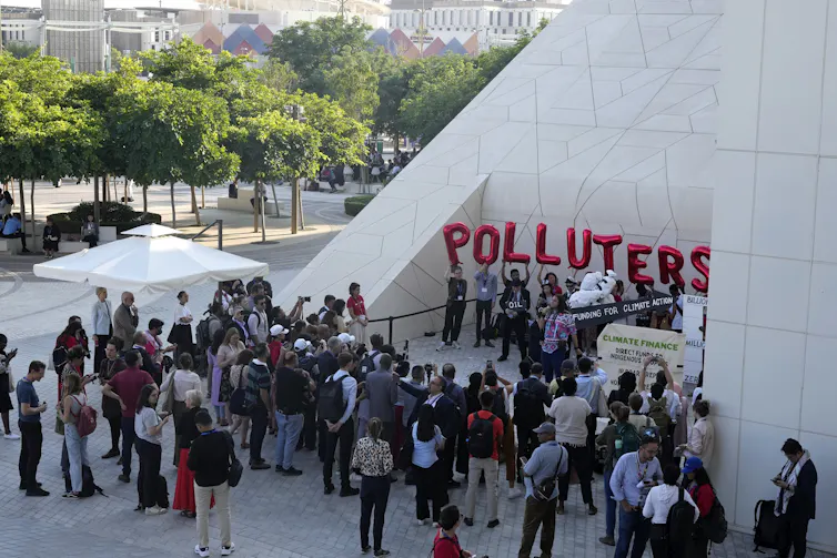 People seen milling around a demonstration where a large sign that says polluters is seen.