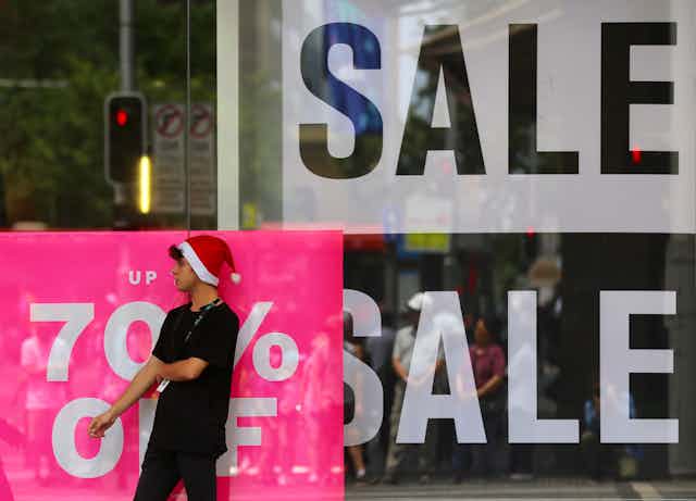 A person in a Santa hat stands in front of a sign saying sale.