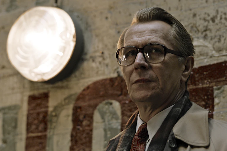 Man in glasses and brown suit, tie and coat looks past the camera