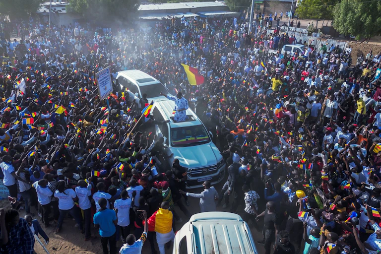 Foule brandissant des drapeaux soudanais autour d'une voiture