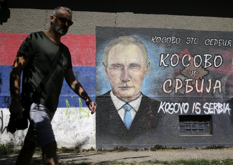 A man walks past a mural showing Russian president Vladimir Putin, reading 'Kosovo is Serbia'.