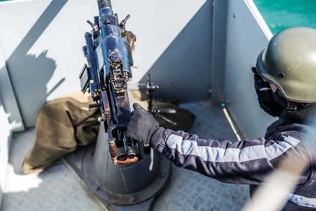 A gloved hand resting on the muzzle of a machine gun facing out into a body of water