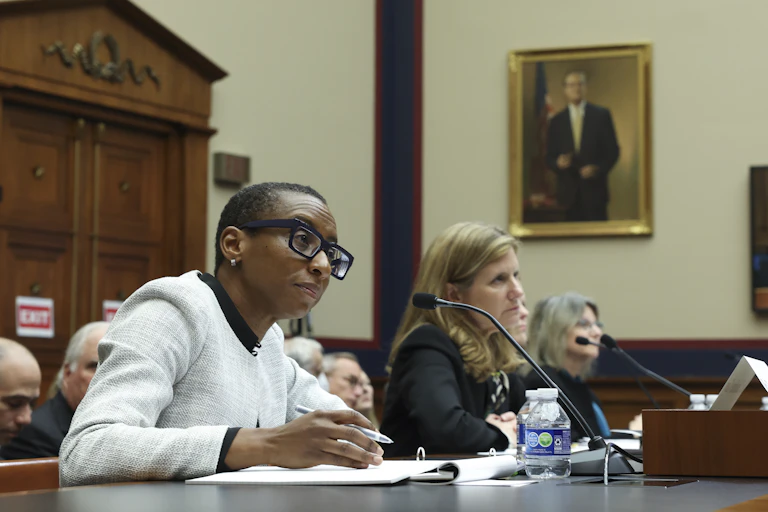 Three women seated at a large table behind microphones.