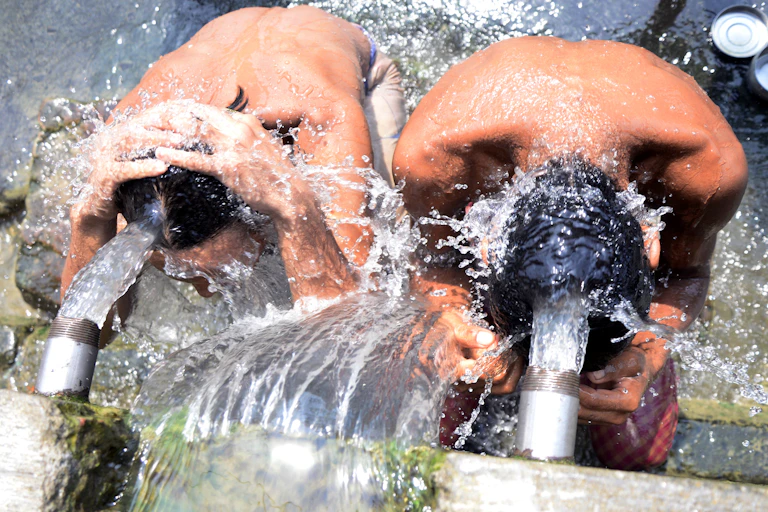 Two boys cooling off under water outflow pipes.