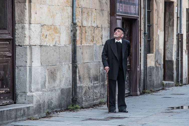 Un hombre pasea solo por la calle y mira hacia arriba, buscando una ventana.